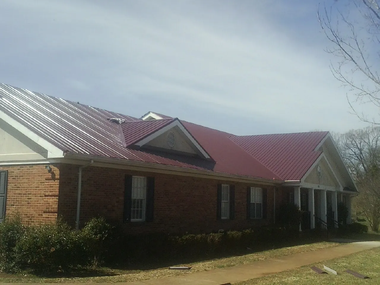 Red metal roof with gabled entries on a long brick building, from a Hail Damage Roof Repair job in Lehighton
