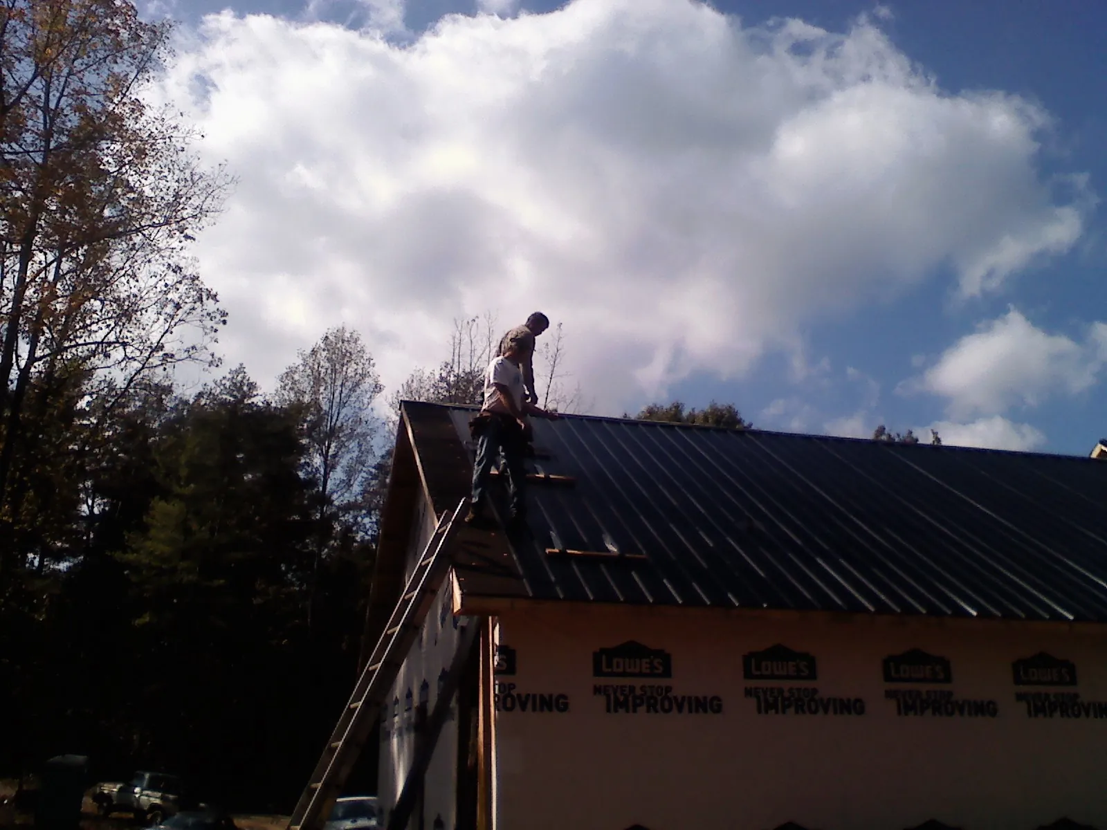 Roofer fastening dark metal panels high against a cloudy sky, from a Roof Inspection job in Lehighton