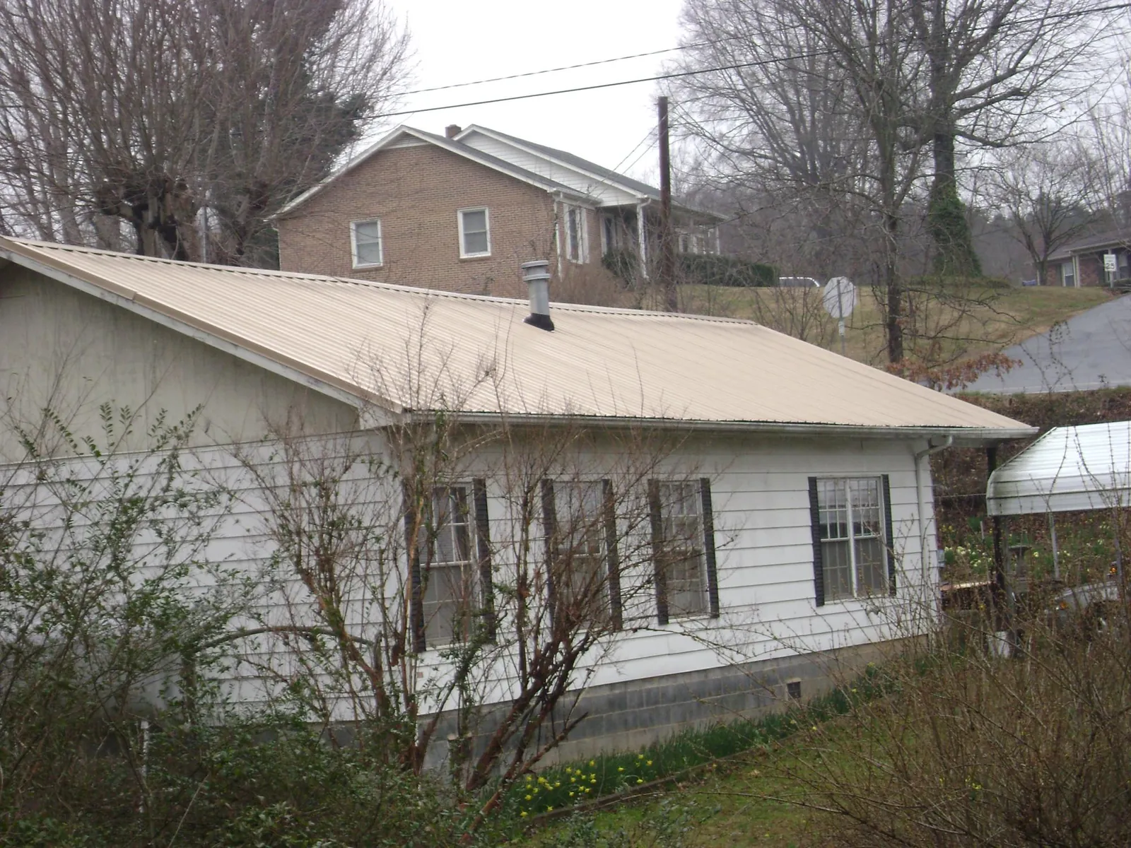 Tan metal roof on a white sided house set into a hillside — Commercial Roofing by Roofing Brothers in Lehighton